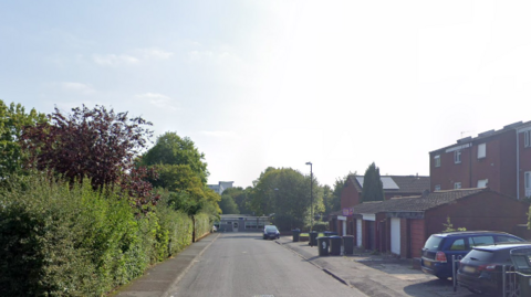 A residential street, lined with red brick houses and green bushes