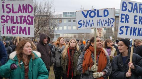 People hold banners and protest in front of Parliament building in Reykjavik