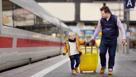 Father and son pulling a suitcase along a train platform