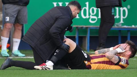 Bradford striker Andy Cook receives treatment on the pitch after being injured at Barrow