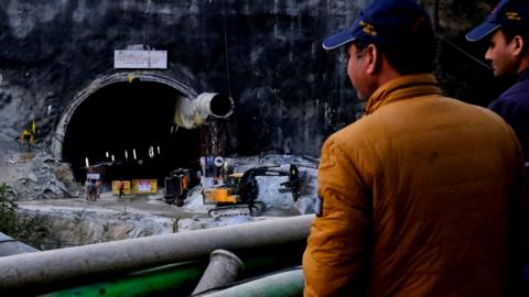 Men overlook the entrance of a tunnel where workers have been trapped for ten days after the tunnel collapsed in Uttarkashi, in the northern state of Uttarakhand, India, on 22 November 2023