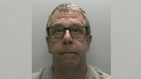 Devon and Cornwall Police mugshot of Peter Wilkinson. He has large black-rimmed glasses on and a grey jumper.