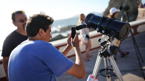 A person takes photos of the sun with a telescope ahead of this Monday's eclipse