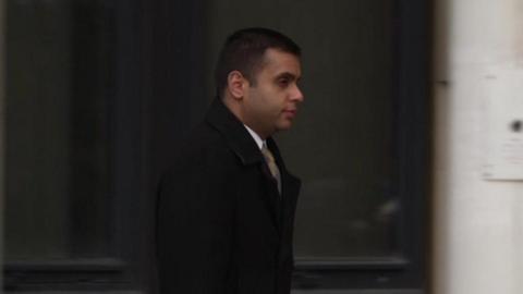 Faisal Shoukat pictured walking away from the court wearing a black overcoat and gold tie. He is carrying a briefcase.
