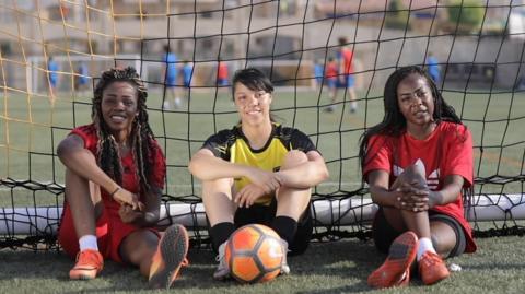 Three Egyptian women footballers sitting in a goal with a ball at their feet
