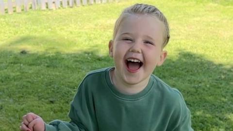 Happy girl wearing green top and blue trousers runs through a garden.