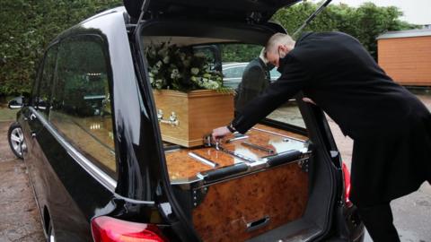 A staff member loads a coffin into a hearse