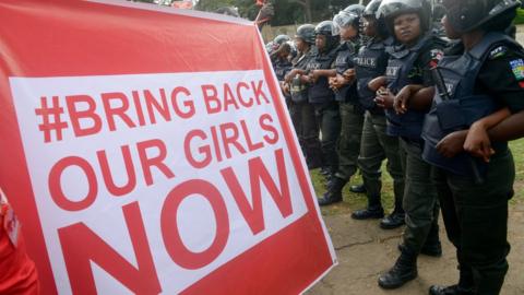 Supporters of the #BringBackOurGirls campaign hold a placard as policewomen block supporters from marching to the president's official residence in Abuja on October 14, 2014.