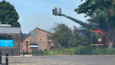 Firefighters on a ladder looking at a smouldering building
