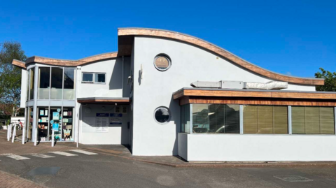 The side of a pale blue health care building, with circular windows and a curved roof.