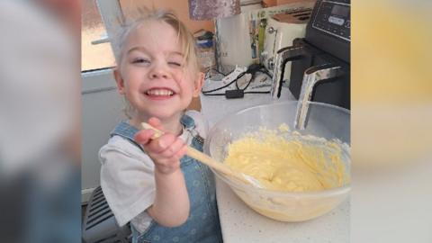 Amelia mixing cake batter in a bowl in her family kitchen. She has a big grin on her face.