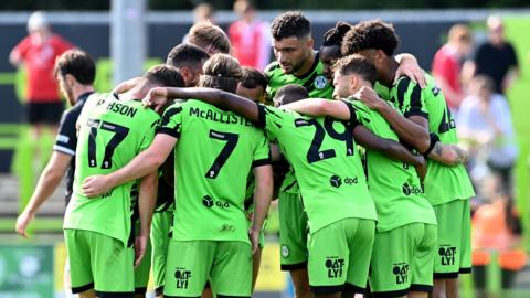 Forest Green players huddle together to celebrate their goal against Crewe