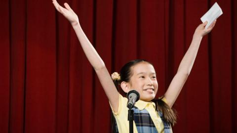 A child celebrates after performing on the stage, with a microphone in front of them.