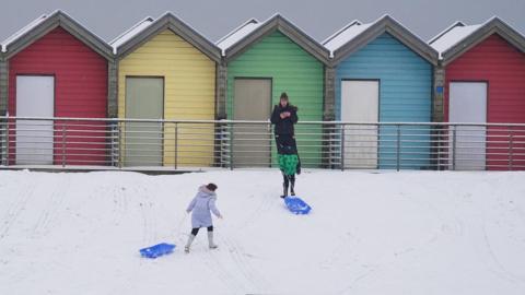People walk through the snow beside the beach huts at Blyth in Northumberland, as temperatures are tipped to plunge to as low as minus 11C in parts of the UK over the weekend.