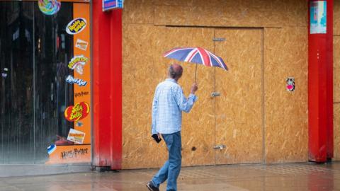 A shopper passes a boarded up shop unit in London