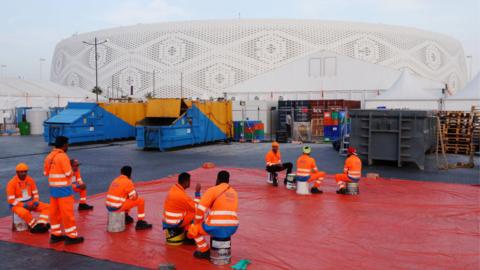A group of workers wearing high vis clothing sit outside Al Thumama Stadium in Qatar