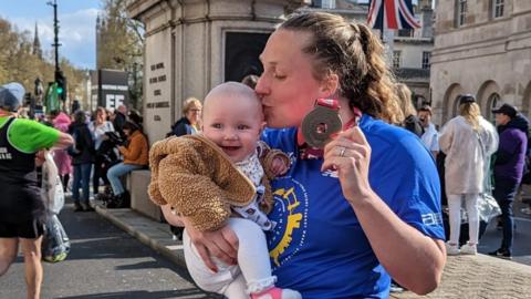 Zoe Jacobs with her baby holding a medal after a run