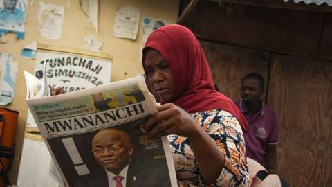 A woman reads a newspaper announcing the death of Tanzania's President John Magufuli in Dar es Salaam, on March 18, 2021.