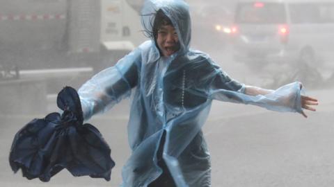 A woman runs in a waterproof with an umbrella in hand in heavy rainstorm in Shenzhen