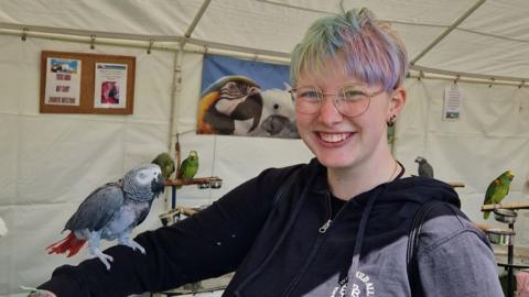 A person with colourful hair holding a bird