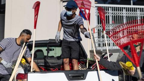 Volunteers collect rakes and other cleaning material during a cleanup operation organised by the Grace Family Church in Durban on 18 July 2021