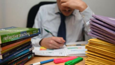 Teacher marking, surrounded by books