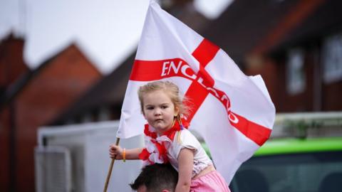 A young girl holds a St George flag at the 2018 Stone Cross St George's Day parade