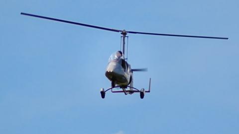 Gyrocopter flying across blue sky