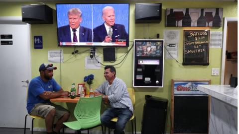 People sitting under screen of Trump Biden debate