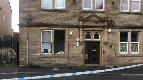 Property cordoned off by police tape with windows blown out after an explosion