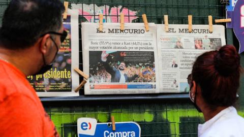 People look at a newspaper´s front page depicting Chilean president-elect Gabriel Boric at a newsstand in Santiago, on December 20, 2021