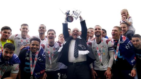 Derby County owner David Clowes hold the promotion trophy aloft while surrounded by players