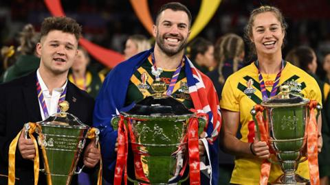 England's Tom Halliwell, Australia's James Tedesco and Australia's Kezie Apps hold the respective World Cup trophies for winning the wheelchair, men's and women's competitions.