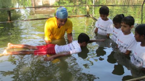 An instructor teaches young children to swim