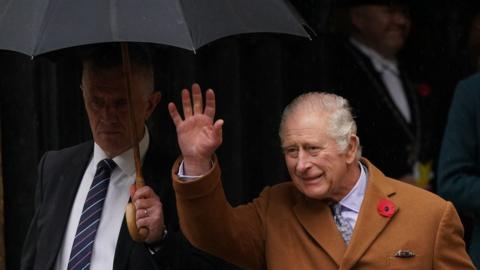 King Charles waving from under an umbrella