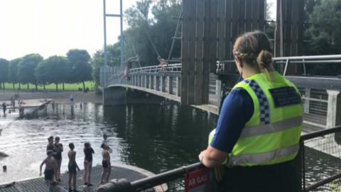 A PCSO looks on as a boy leaps into the water