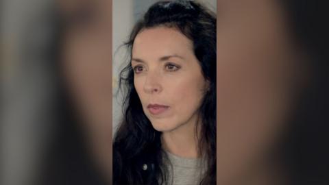 A woman looks annoyed. She has long brown hair.