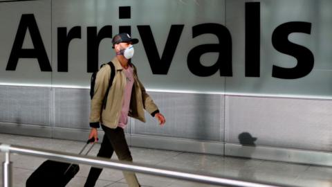 A man wearing a mask pulls his suitcase through an airport