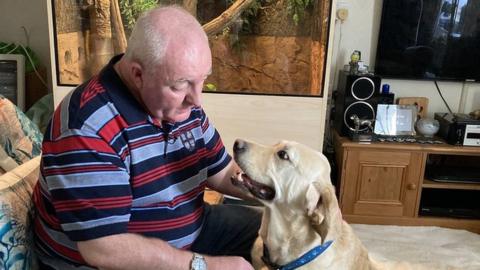 Alex Gosney at home talking to his guide dog Homer