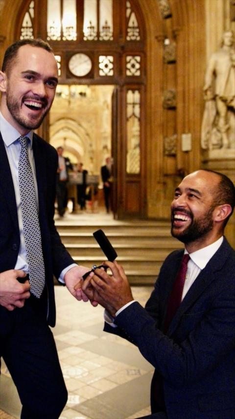 A man in a suit proposing to another man in a suit.