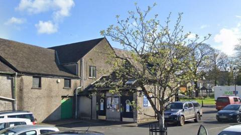 The public toilets at The Square, in Milnthorpe. It is a pebble-dashed building next to a car park.