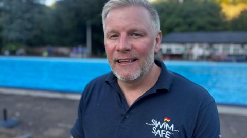 Scott Clayton, in a Swim Safe polo shirt, stood in front of New Bath Lido, looking at the camera