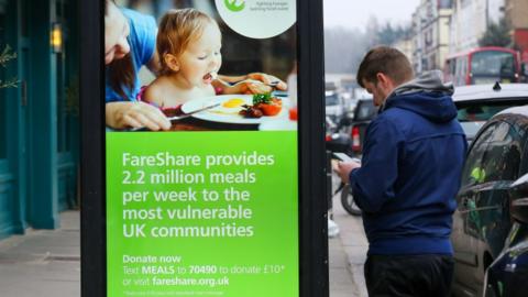 A man stands next to FareShare digital advert.