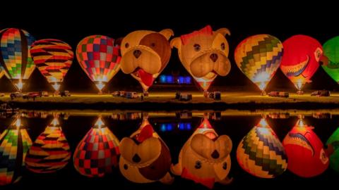 hot air balloons lined up at night and reflected in water