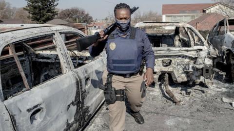 - A Johannesburg Metro Police Department (JMPD) officer walks between burnt cars at a car showroom in Jeppestown, Johannesburg, on July 11, 2021.