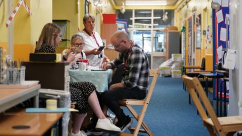 Head teacher Caroline Evans and staff members sit in a temporary staff room in the corridor of Parks Primary School in Leicester