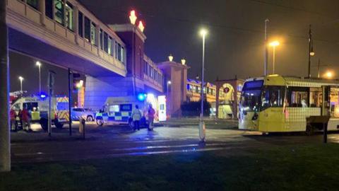 A photo of the scene of a collision between a tram and a car. The photo shows police vehicles parked under a bridge and a tram parked nearby.