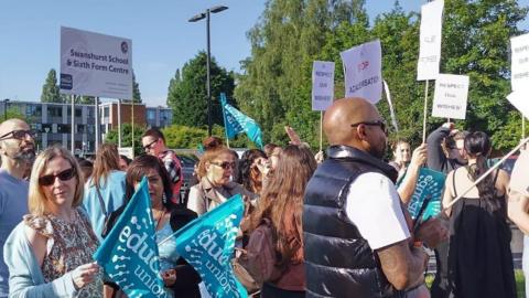 Male and female union members stood outside Swanshurt School with placards