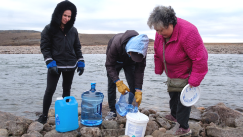 Emily and Cory Shoapik help Lucy Mingeriak fill containers with water from the Sylvia Grinnell River