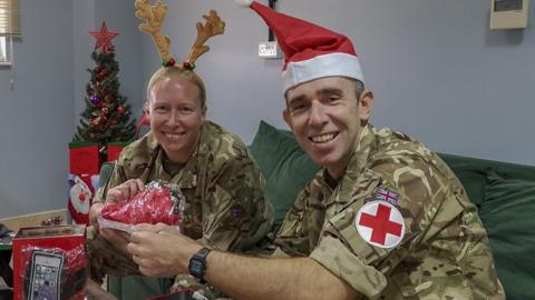 Two members of the armed forces wearing Christmas-themed headwear